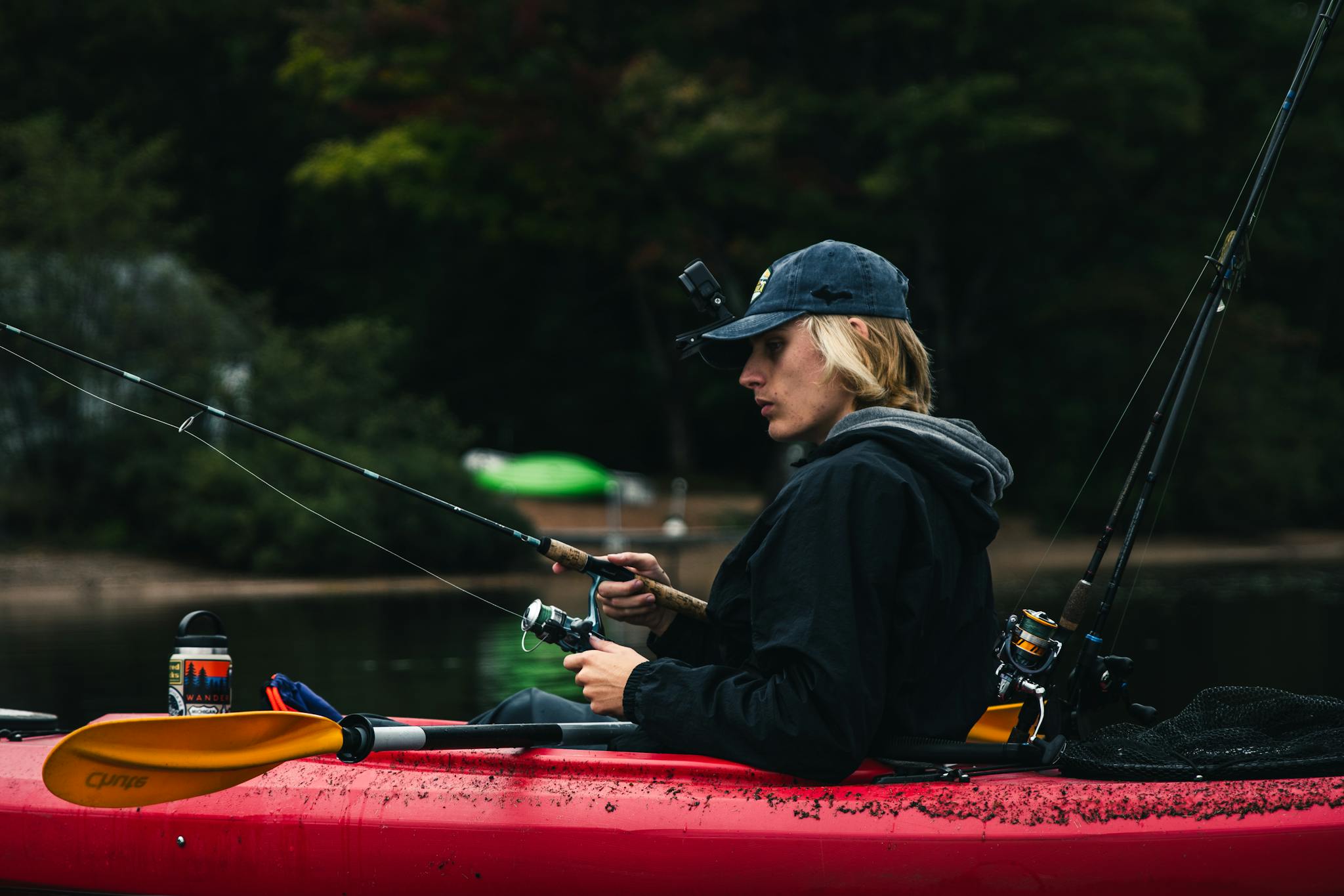 A man fishing from a kayak in a serene lake, surrounded by lush greenery.